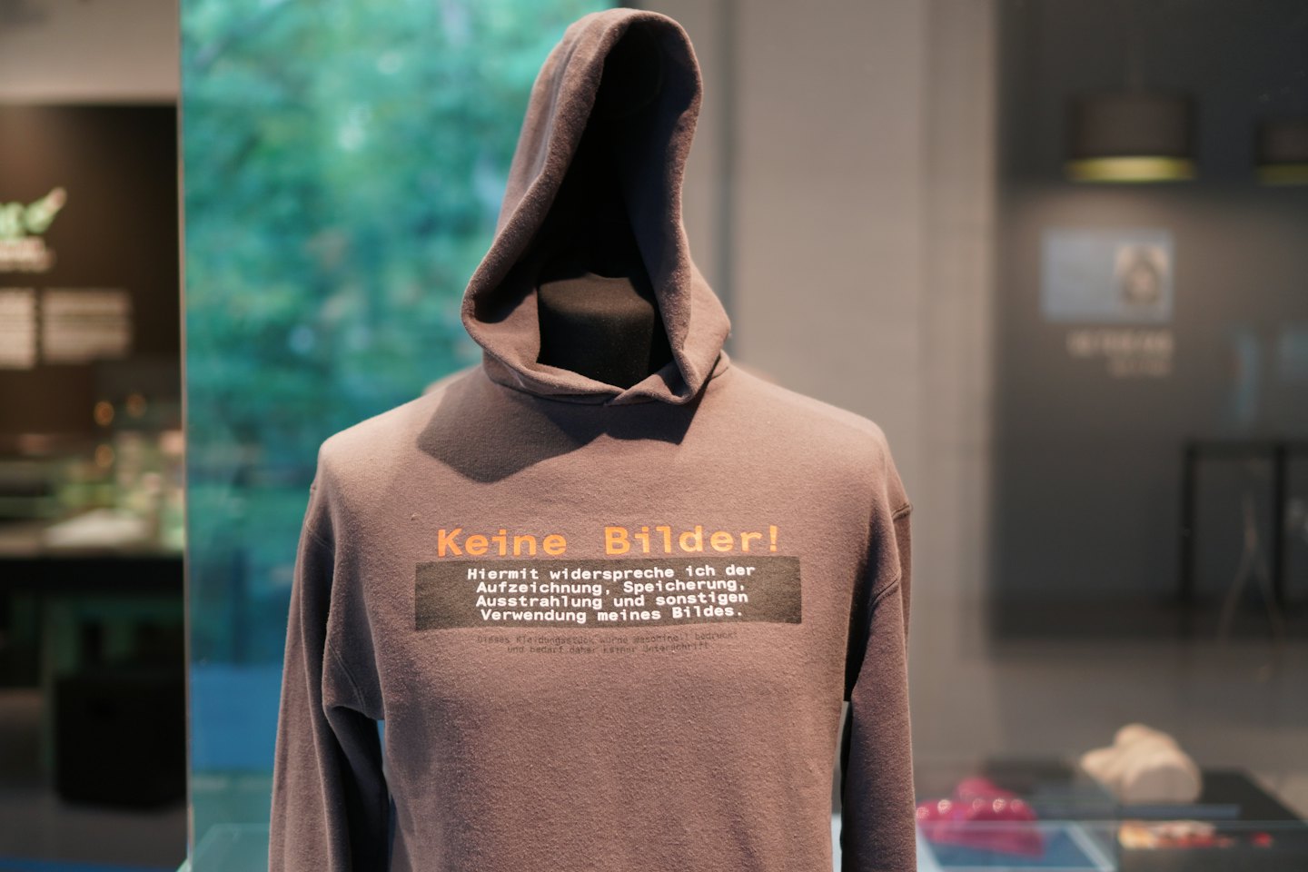Grauer Kapuzenpullover mit orange-weißer Schrift auf einer Schaufensterpuppe.