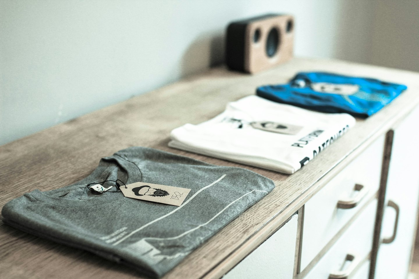 Graue, weiße und blaue gefaltete T-Shirts liegen auf einer Kommode.