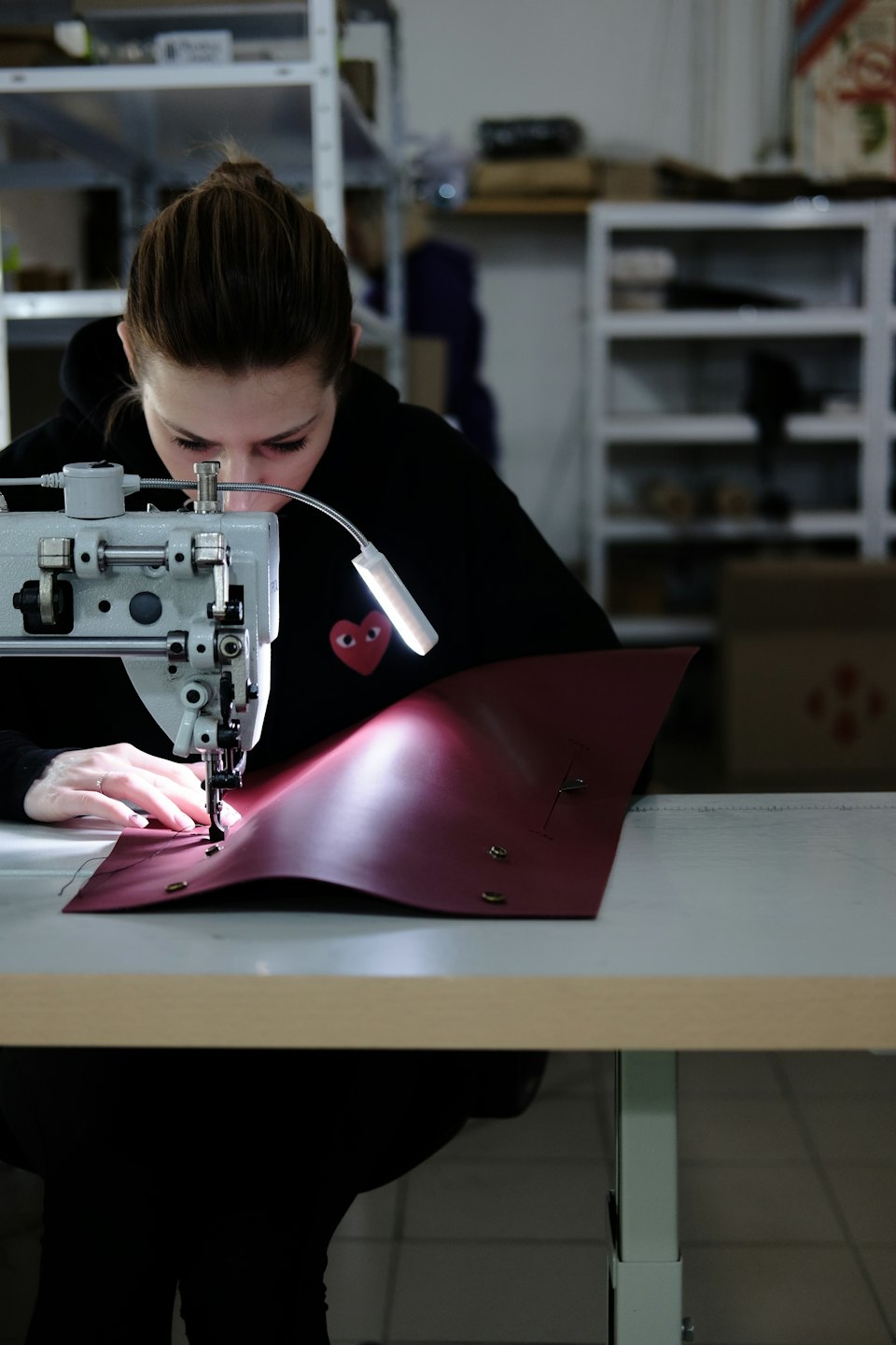 Frau näht rotes Leder auf einer Nähmaschine.