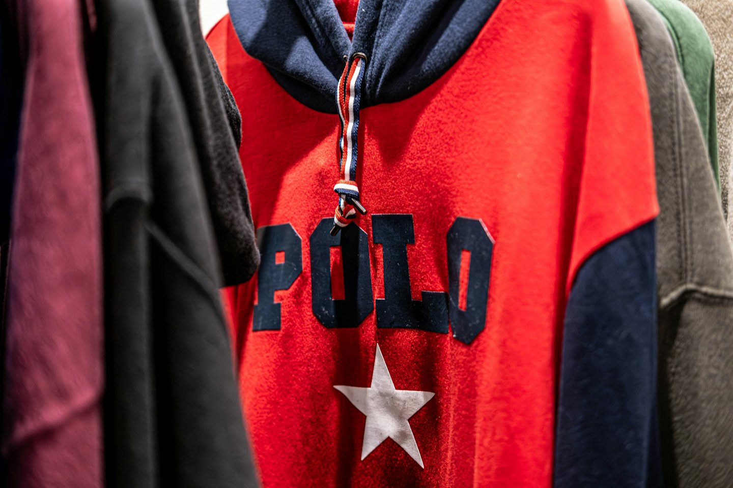 Roter Kapuzenpullover mit dunkelblauen Akzenten, der an einer Kleiderstange hängt.